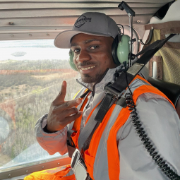 Portrait of grad student Sam Tetteh giving peace sign in a helicopter